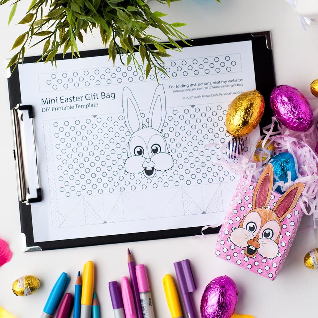 A template for do it yourself easter baskets, laying flat attached to a clipboard with pencils, markers and chocolate easter eggs scattered beside.