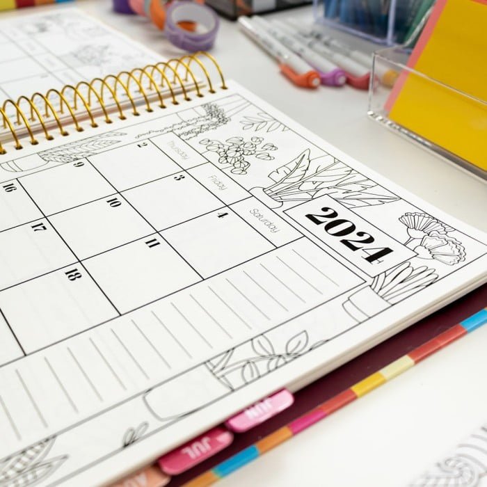 Open scratch-resistant hardcover 2024 Coloring Planner displaying house plant weekly spread page and colorful stationary